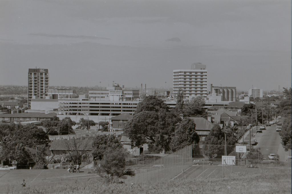 View of Grace Bros, and Council building from Parramatta Park near the intersection of Pitt and Campbell streets, with basketball court in foreground. Circa 1977. City of Parramatta Archives: ACC002/107/025