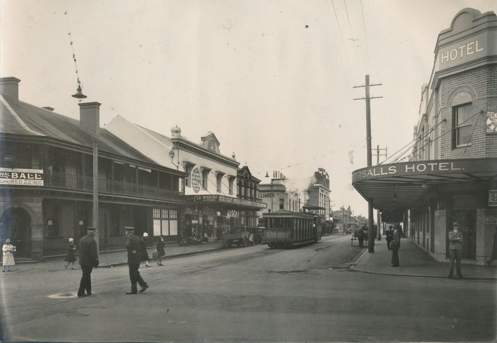 The corner of Church and George Streets circa 1920s - 1930s. This view of George Street includes the Tattersall's Hotel on the right (now the 7-Eleven) and the Old Bank of New South Wales Building on the left. Further down the street, you can see a "Fur Coat, Stole and Rug" Store and a Printers and Publishers.  Photo album of Sydney Davies, City of Parramatta Archives: ACC198/038